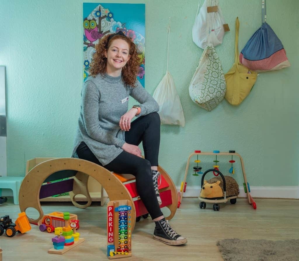 a childcare practitioner sits in a nursery surrounded by toys