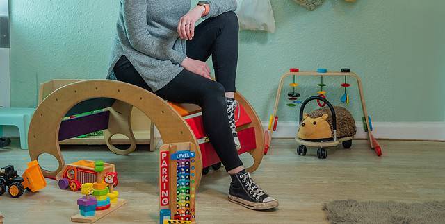 a childcare practitioner sits in a nursery surrounded by toys