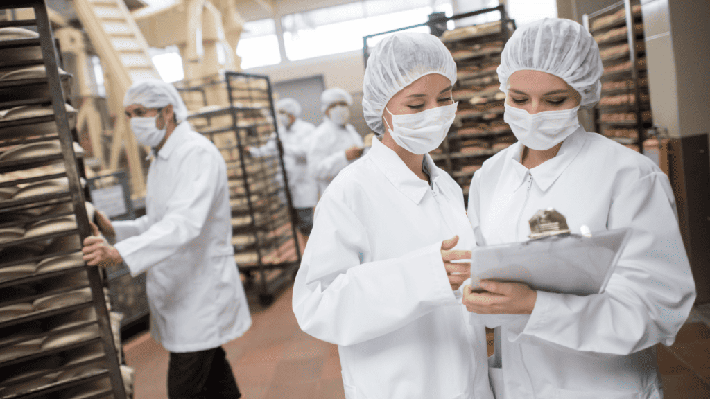 workers in hair nets, masks and lab coats working in a commercial kitchen.