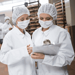 workers in hair nets, masks and lab coats working in a commercial kitchen.