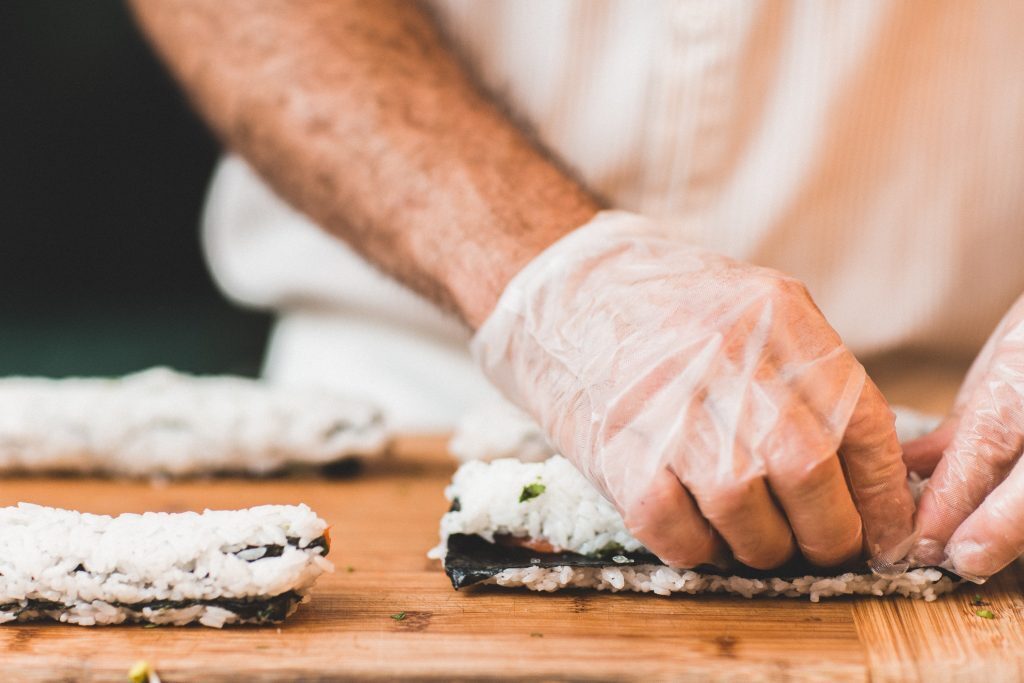 A person prepares sushi rolls while wearing gloves