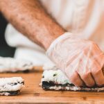 A person prepares sushi rolls while wearing gloves