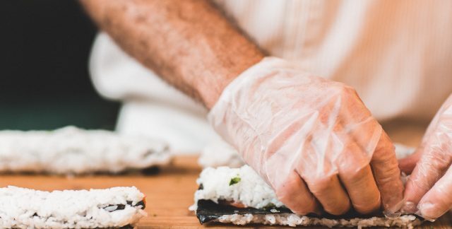 A person prepares sushi rolls while wearing gloves