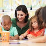 A woman caring for several children doing an activity at a desk