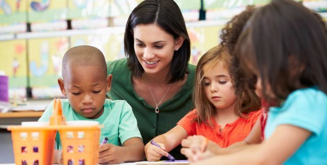 A woman caring for several children doing an activity at a desk