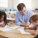 A male childcare practitioner helps children working on an activity in a classroom