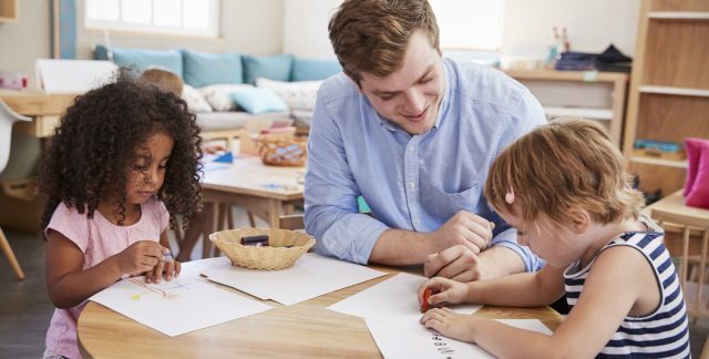 A male childcare practitioner helps children working on an activity in a classroom