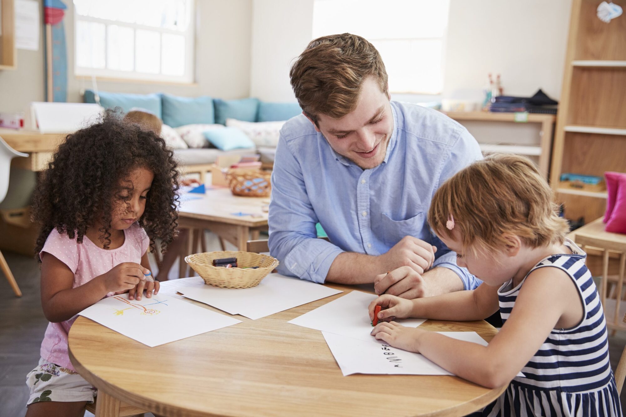 A male childcare practitioner helps children working on an activity in a classroom