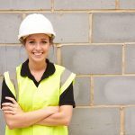 A young woman in a hard hat and high visibility jacket by a concrete brick wall