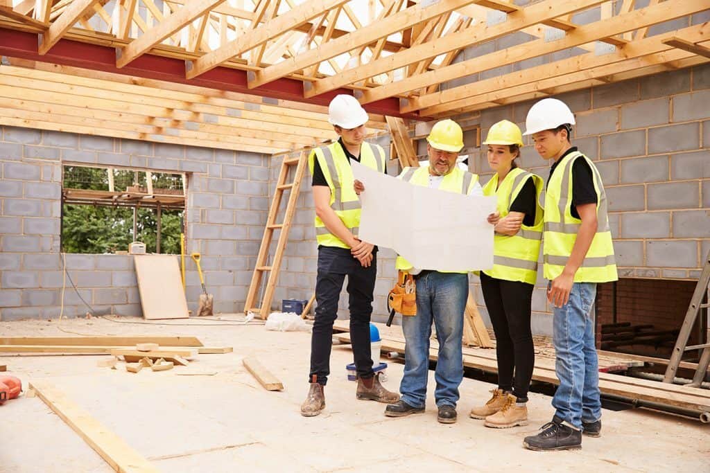 A group of construction workers around a plan in a building site.