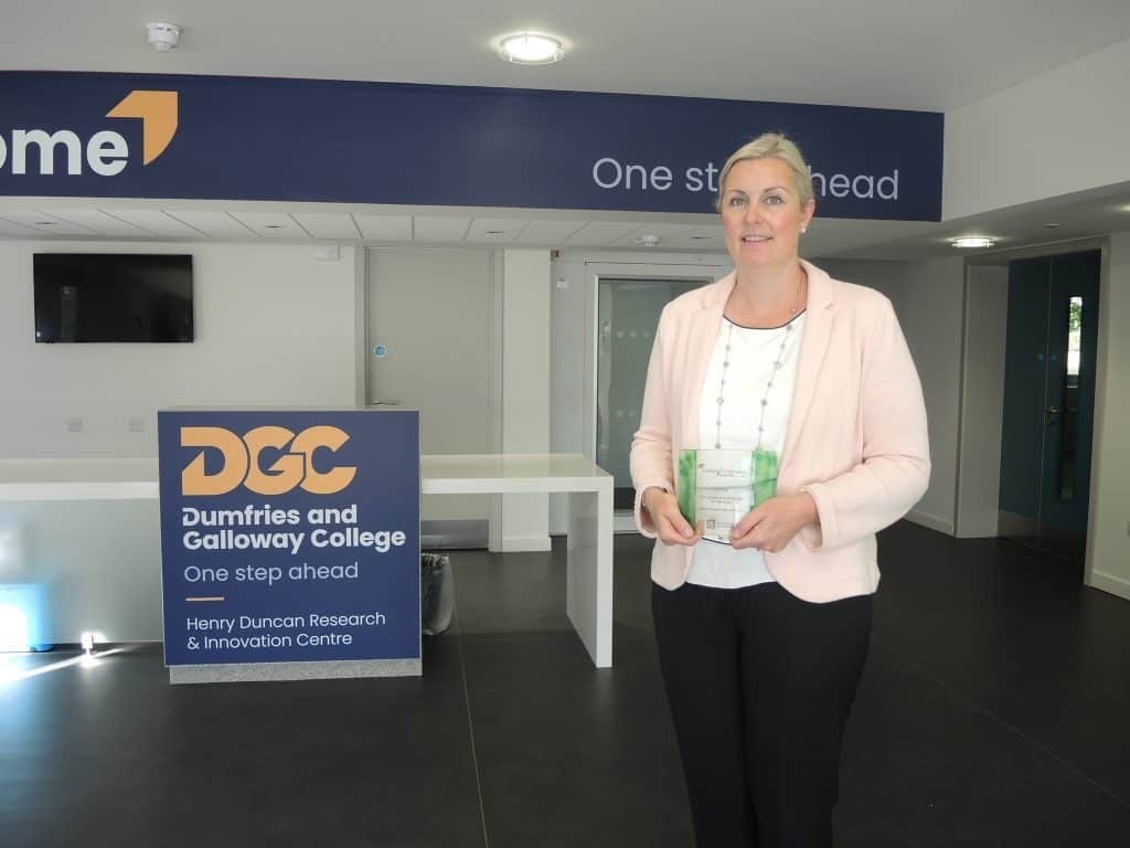 Principal of Dumfries and Galloway College Joanna Campbell holding a green gown award in the Henry Duncan Building at Dumfries Campus