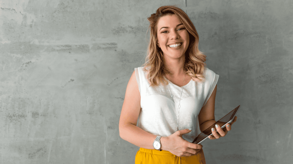 A smiling woman in work clothes holding a tablet