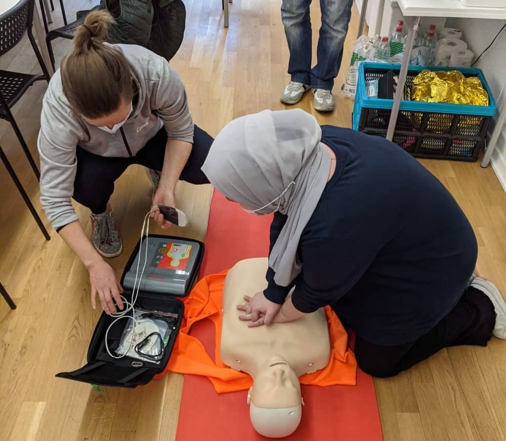 Students performing CPR and defibrillation on a dummy in a classroom