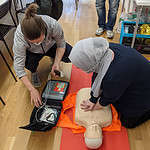 Students performing CPR and defibrillation on a dummy in a classroom