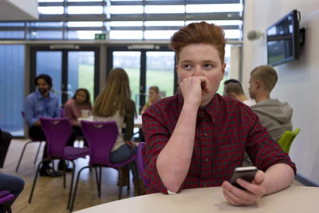 A boy looking reflective at a table. Behind him are other children.