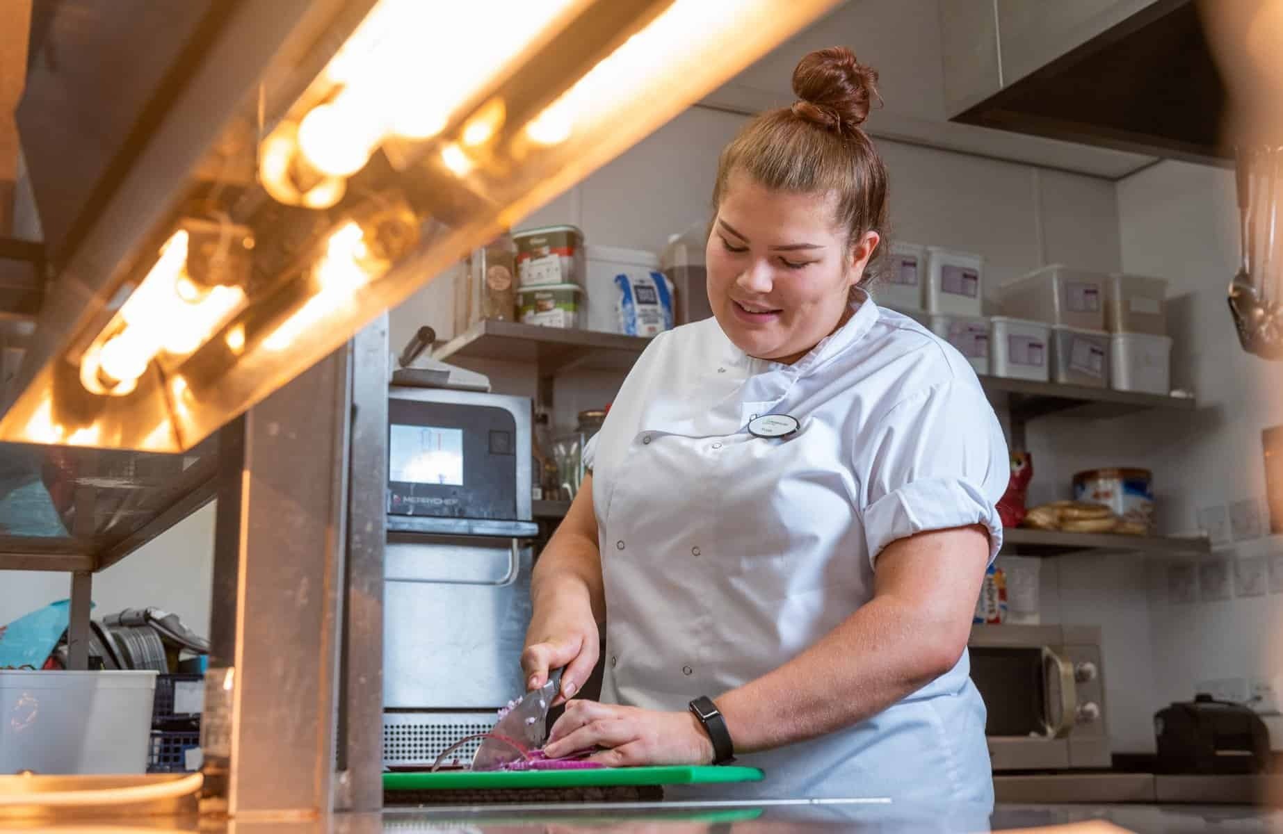 An apprentice chef chopping up vegetables in a commercial kitchen