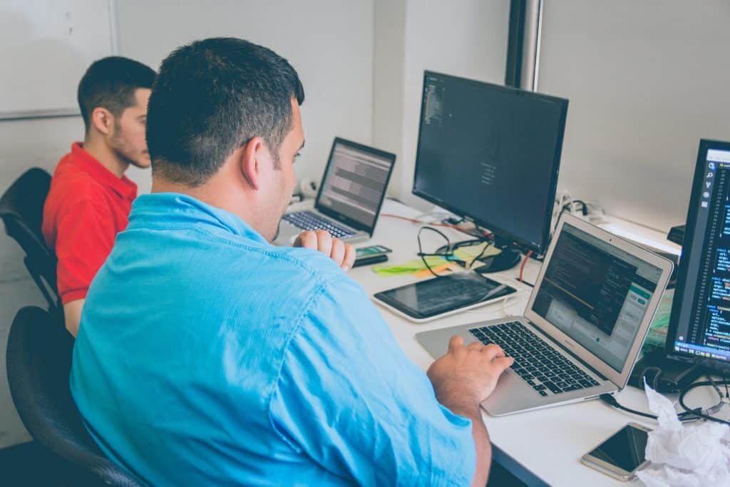 A man codes at a laptop computer in a classroom.