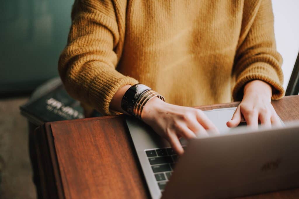 A person in a mustard coloured jumper uses a laptop