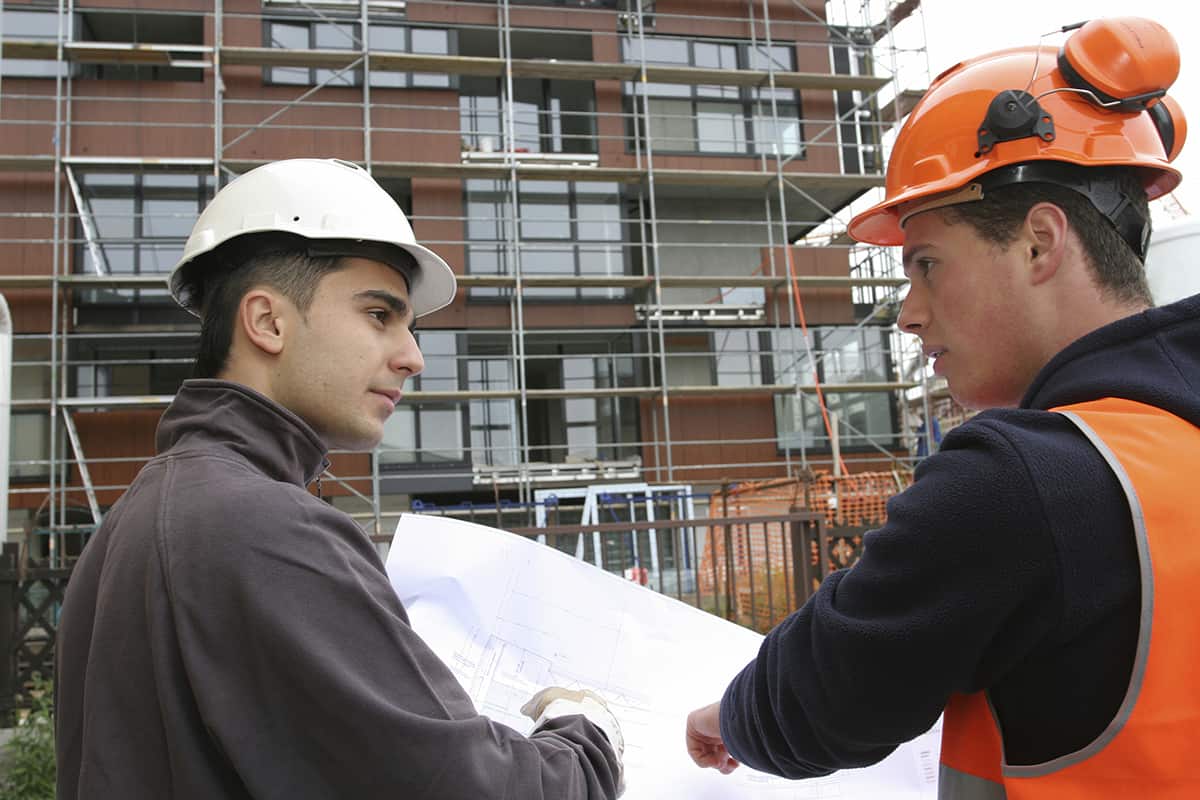 Two construction workers look at a building plan on a building site