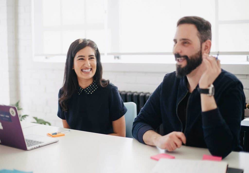 A smiling woman and man sitting at a meeting table with a laptop