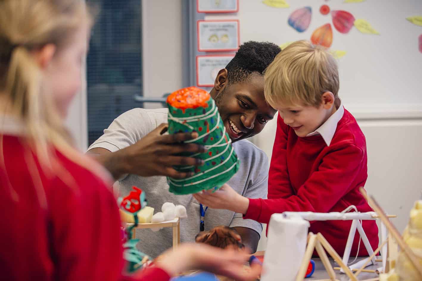 A male childcare practitioner helping a group of children with an activity.