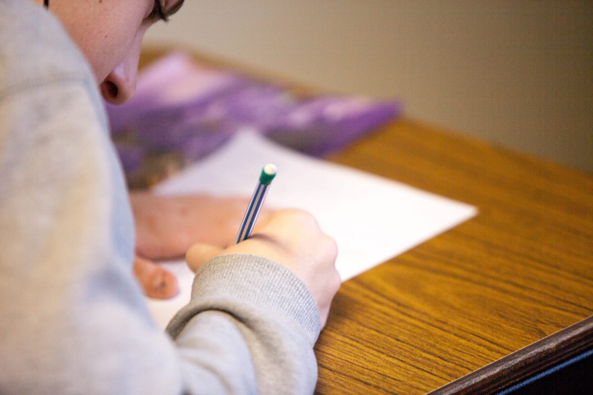 A student writing on a piece of paper lying on a desk while studying.