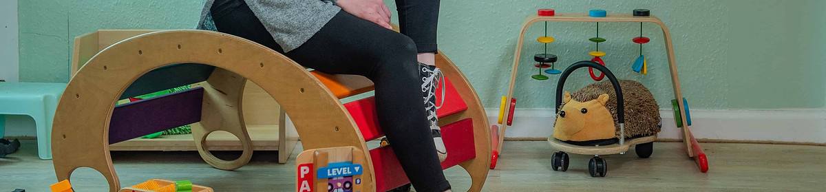 a childcare practitioner sits in a nursery surrounded by toys