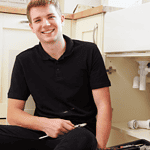 Young male plumbing student working under kitchen sink.