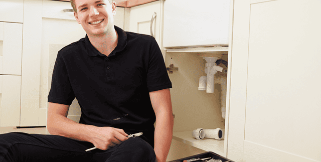 Young male plumbing student working under kitchen sink.