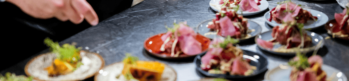 Several small plates of food are arranged on a counter, with a person's hand reaching for one of the plates.